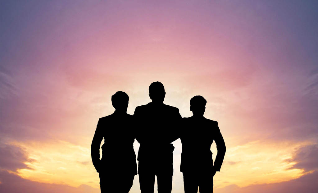 Das Bild zeigt eine Silhouette von drei Personen auf einem Hügel, die sich gegen den Himmel aussehen. Es ist ein Abend- oder Morgenlicht mit einer rosa Farbtonation und einem dunklen Himmel. //